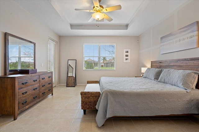 bedroom with a raised ceiling, a textured ceiling, ceiling fan, and multiple windows