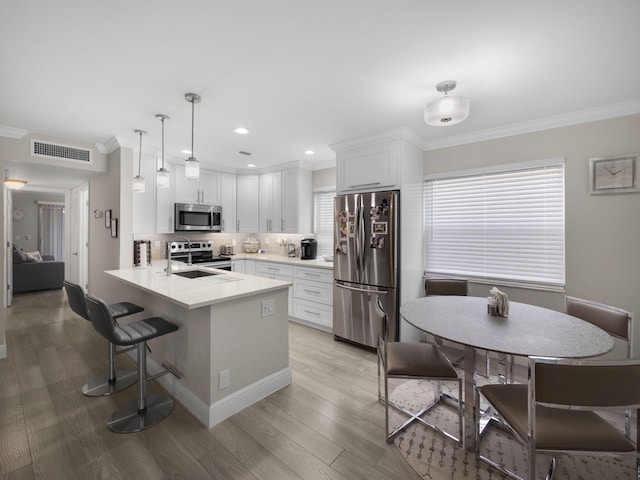 kitchen with tasteful backsplash, decorative light fixtures, appliances with stainless steel finishes, kitchen peninsula, and white cabinets