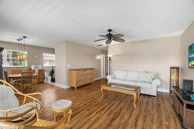 living room with a textured ceiling, dark wood-type flooring, and ceiling fan