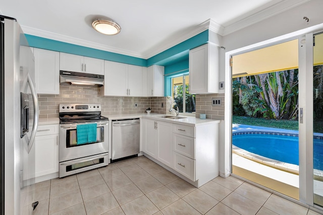 kitchen featuring under cabinet range hood, stainless steel appliances, light countertops, backsplash, and crown molding