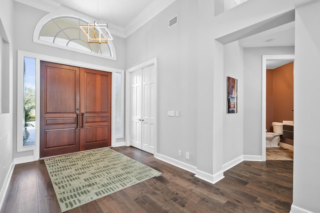 foyer with dark wood-type flooring, a towering ceiling, ornamental molding, and an inviting chandelier