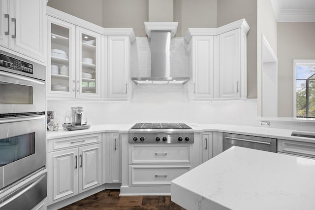 kitchen featuring appliances with stainless steel finishes, tasteful backsplash, white cabinets, crown molding, and wall chimney range hood