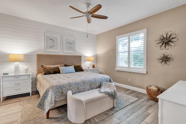 bedroom with wood walls, ceiling fan, and light wood-type flooring