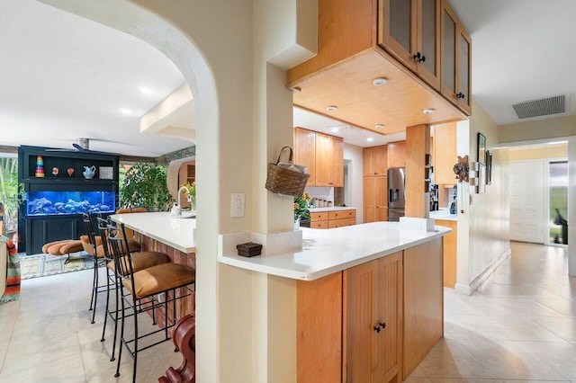 kitchen featuring light tile patterned flooring, stainless steel fridge with ice dispenser, a breakfast bar area, and kitchen peninsula