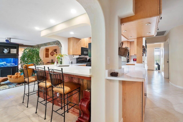 kitchen with light brown cabinetry, sink, a breakfast bar area, kitchen peninsula, and black appliances