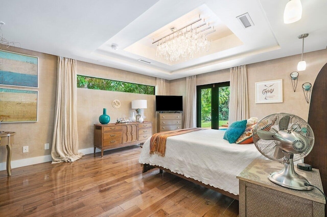 bedroom with a notable chandelier, hardwood / wood-style flooring, a raised ceiling, and french doors