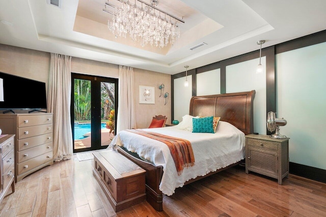 bedroom featuring french doors, access to exterior, light wood-type flooring, and a tray ceiling