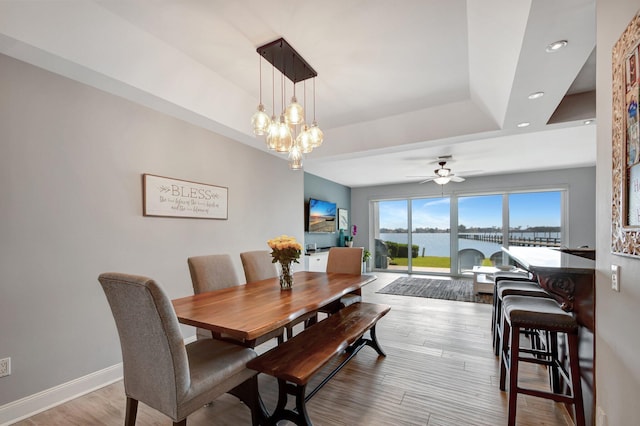 dining space with a tray ceiling, ceiling fan with notable chandelier, and light hardwood / wood-style floors