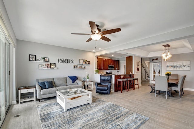 living room featuring ceiling fan with notable chandelier and light wood-type flooring