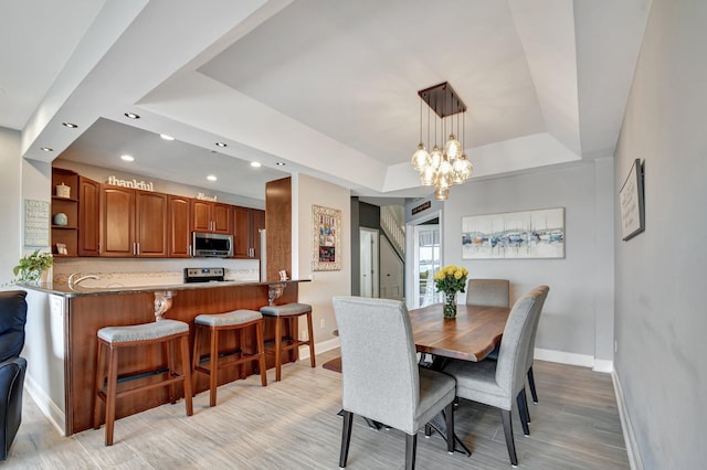 dining room featuring a tray ceiling, a chandelier, and light hardwood / wood-style flooring