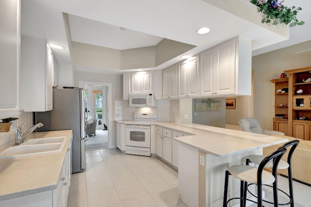 kitchen featuring a breakfast bar, sink, kitchen peninsula, white appliances, and white cabinets