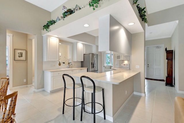 kitchen featuring stainless steel fridge, a breakfast bar area, white cabinets, light tile patterned flooring, and kitchen peninsula