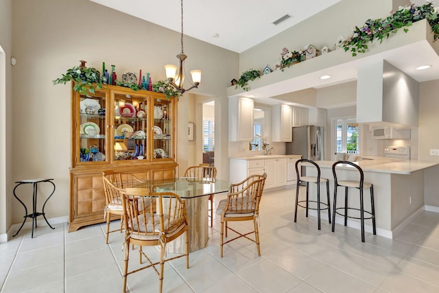 tiled dining space with sink, a notable chandelier, and a towering ceiling