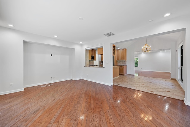 unfurnished living room featuring a notable chandelier and light wood-type flooring