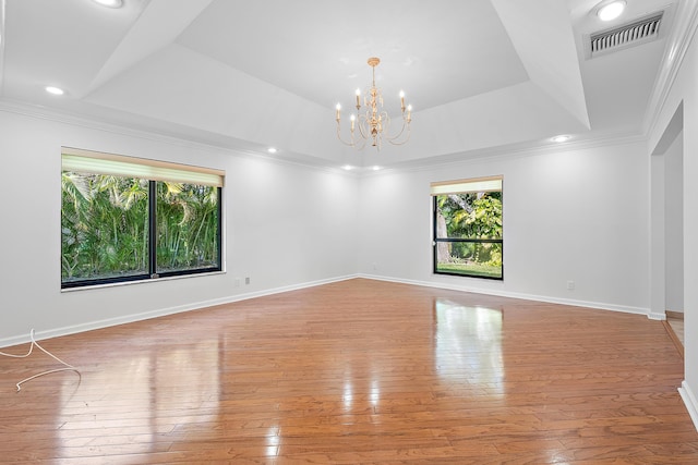 empty room featuring an inviting chandelier, a tray ceiling, light hardwood / wood-style flooring, and crown molding