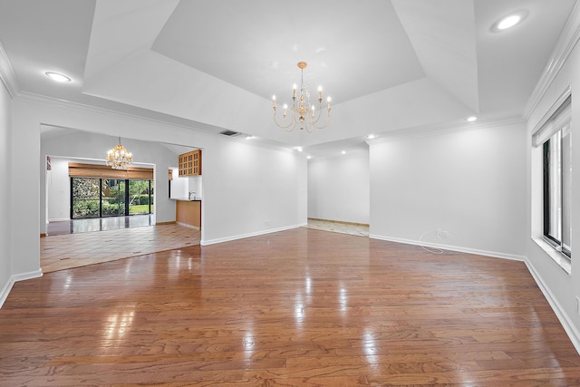 unfurnished living room featuring hardwood / wood-style flooring, ornamental molding, a notable chandelier, and a tray ceiling