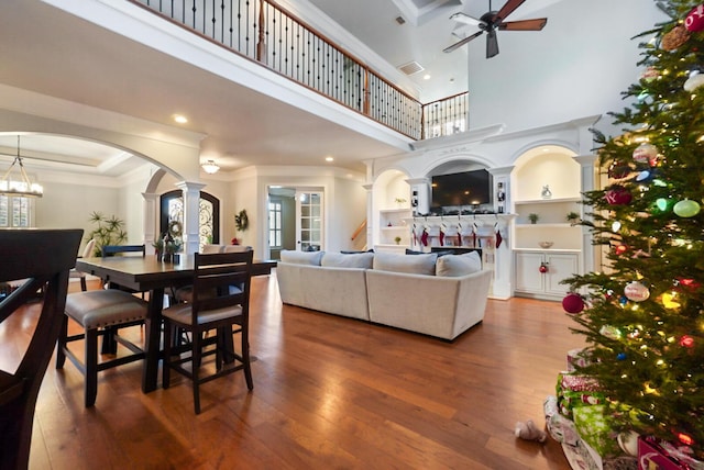 living room with built in features, hardwood / wood-style flooring, ceiling fan, decorative columns, and a high ceiling