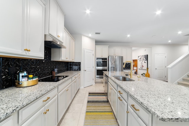 kitchen with sink, light tile patterned floors, appliances with stainless steel finishes, a kitchen island with sink, and white cabinetry