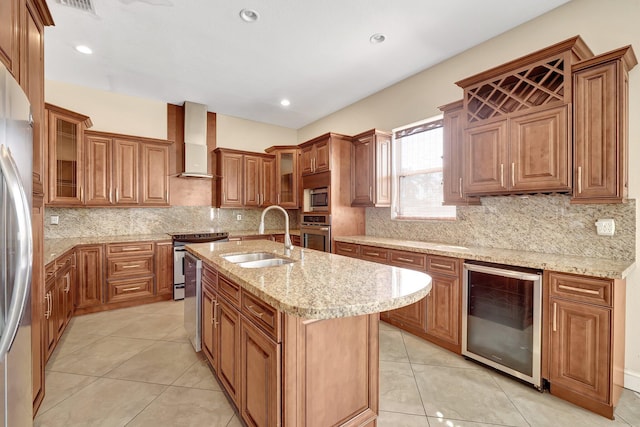 kitchen featuring an island with sink, sink, beverage cooler, stainless steel appliances, and wall chimney range hood