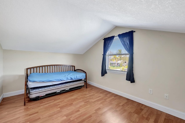 bedroom with vaulted ceiling, hardwood / wood-style floors, and a textured ceiling