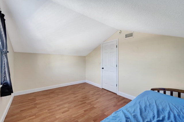 bedroom featuring lofted ceiling, hardwood / wood-style floors, and a textured ceiling