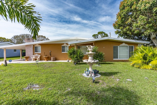 back of house with a carport, a chimney, a yard, and stucco siding