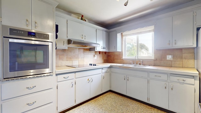 kitchen featuring light countertops, stainless steel oven, under cabinet range hood, and a sink