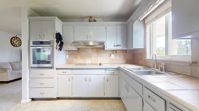 kitchen featuring oven, under cabinet range hood, a sink, and backsplash