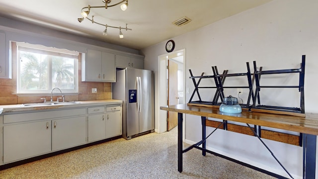 kitchen with light countertops, backsplash, visible vents, a sink, and stainless steel fridge
