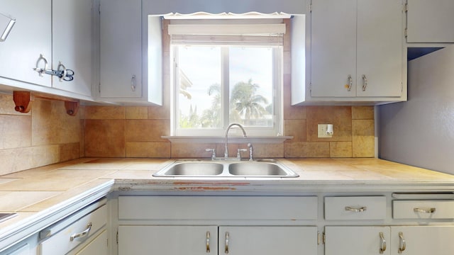 kitchen featuring tile counters, sink, and white cabinets