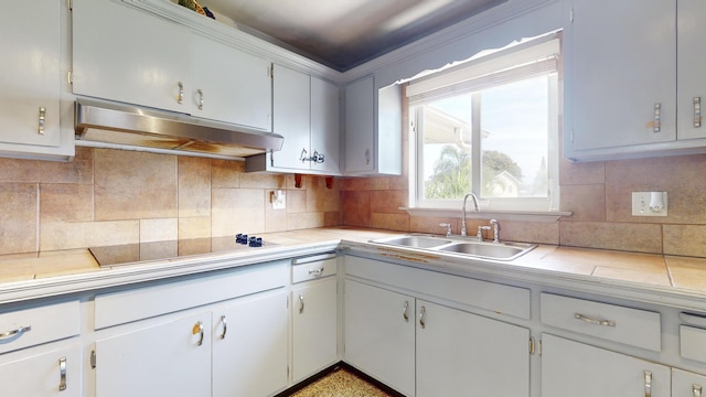 kitchen with tasteful backsplash, white cabinetry, sink, and tile countertops