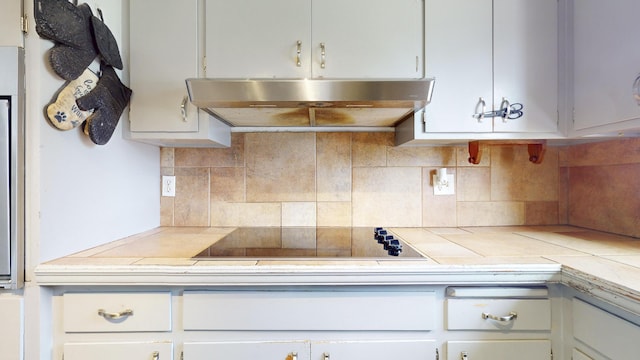 kitchen with tasteful backsplash, black electric stovetop, tile counters, and white cabinets