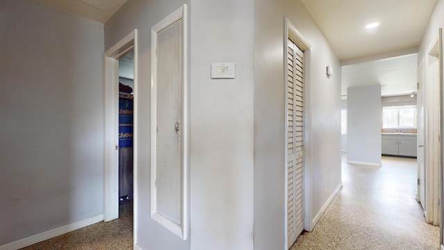 corridor featuring speckled floor, baseboards, and a sink