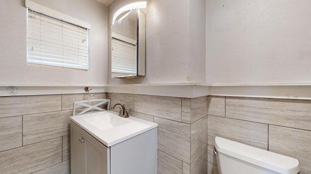 bathroom with tile walls, a wainscoted wall, vanity, and toilet