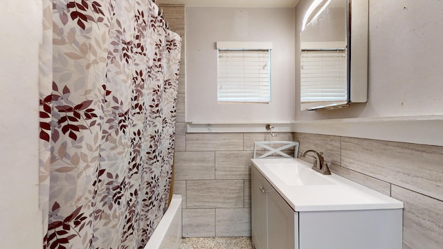 full bath with shower / bath combo, tile walls, wainscoting, speckled floor, and vanity