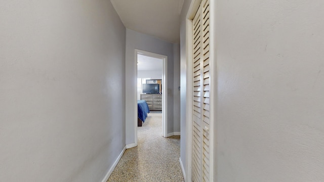 hallway featuring speckled floor and baseboards