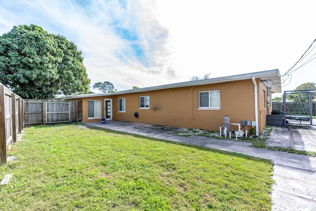 rear view of property with stucco siding, a lawn, a fenced backyard, and a patio