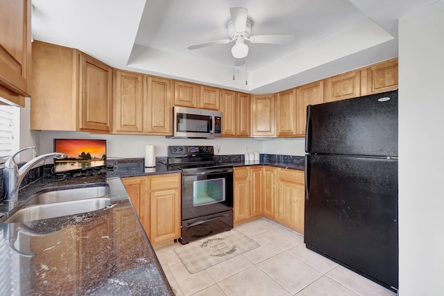 kitchen featuring sink, dark stone counters, light tile patterned floors, black appliances, and a raised ceiling