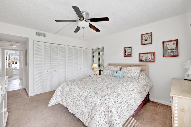 bedroom with multiple closets, ceiling fan, light carpet, and a textured ceiling