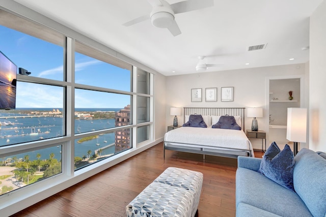 bedroom with a water view, ceiling fan, hardwood / wood-style floors, and multiple windows