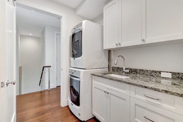 washroom with cabinets, stacked washer / drying machine, sink, and light hardwood / wood-style flooring