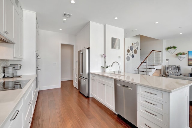 kitchen with appliances with stainless steel finishes, sink, white cabinets, dark hardwood / wood-style flooring, and a kitchen island with sink