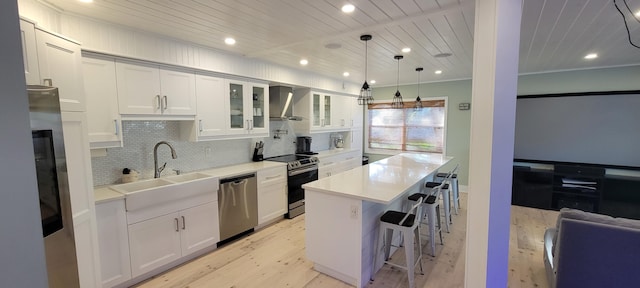 kitchen with stainless steel appliances, a center island, white cabinets, and wall chimney exhaust hood