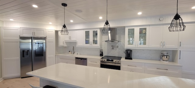 kitchen featuring pendant lighting, wall chimney range hood, appliances with stainless steel finishes, white cabinetry, and decorative backsplash