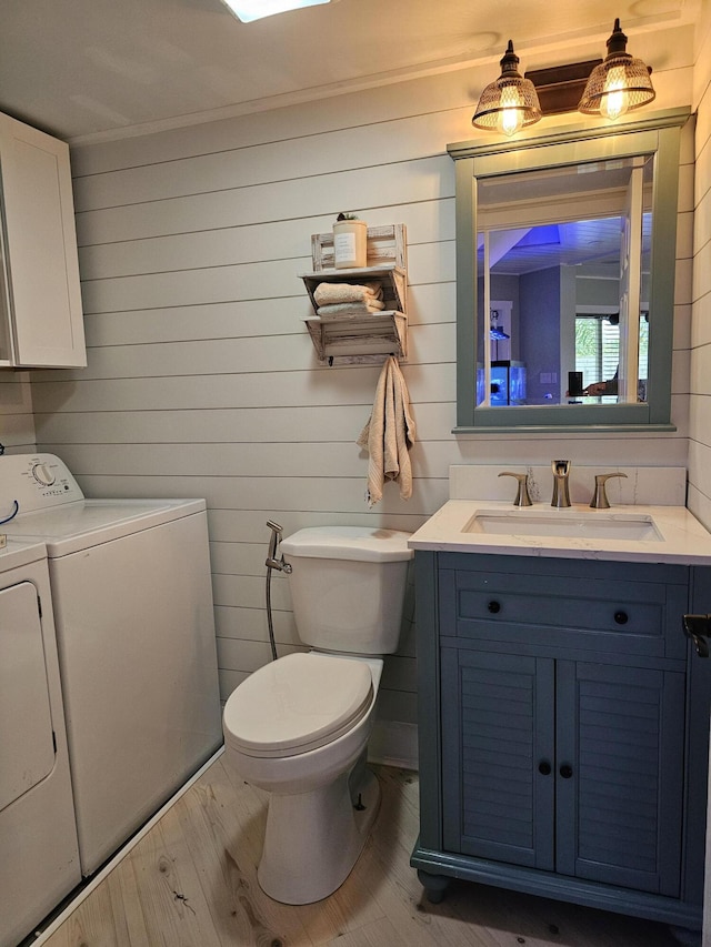 bathroom with hardwood / wood-style flooring, wooden walls, vanity, washing machine and clothes dryer, and toilet