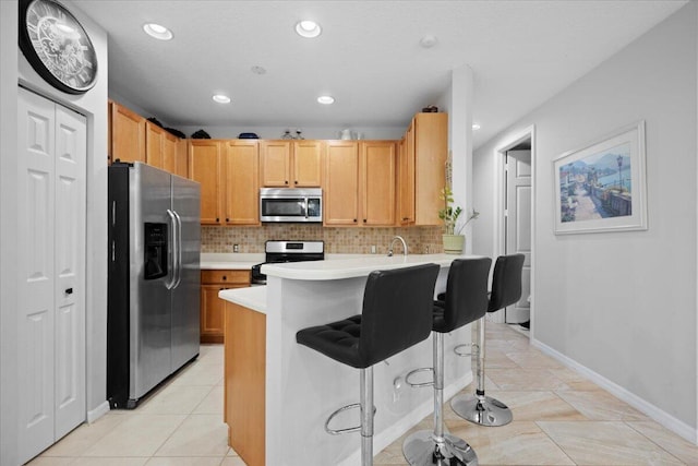 kitchen with light tile patterned floors, a breakfast bar area, appliances with stainless steel finishes, tasteful backsplash, and kitchen peninsula