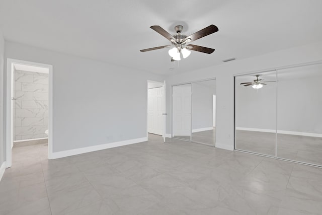 unfurnished bedroom featuring multiple closets, ensuite bath, and ceiling fan