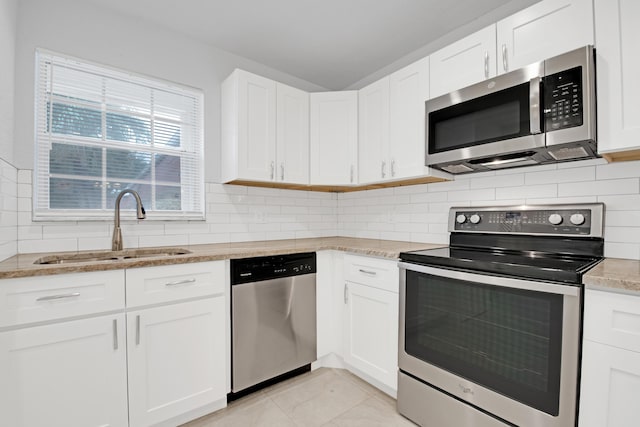 kitchen featuring appliances with stainless steel finishes, sink, white cabinets, decorative backsplash, and light tile patterned floors