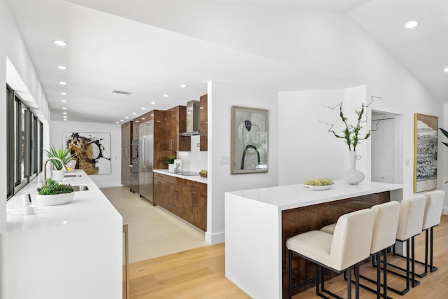 kitchen with a breakfast bar, sink, a kitchen island with sink, wall chimney range hood, and light hardwood / wood-style flooring