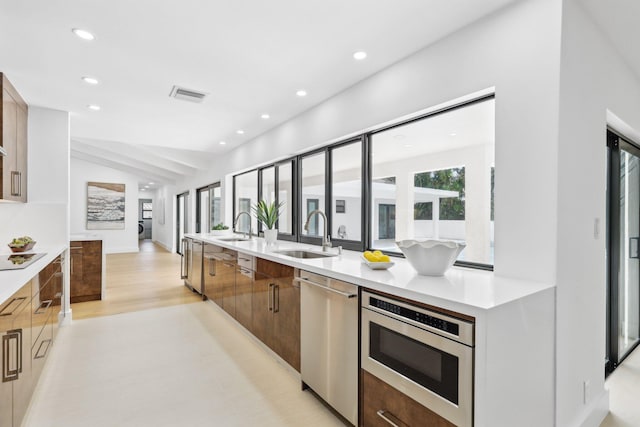 kitchen with lofted ceiling, appliances with stainless steel finishes, light hardwood / wood-style floors, and sink